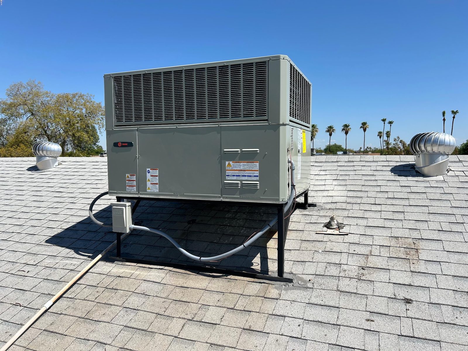 A new Trane rooftop package unit set on a stand on a shingle roof in Phoenix, with the electrical whip and disconnect fitted.