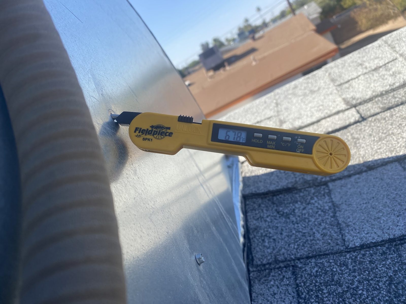 A Fieldpiece SPK1 probe thermometer inserted into a supply plenum on a rooftop, reading 67.8 degrees Fahrenheit.
