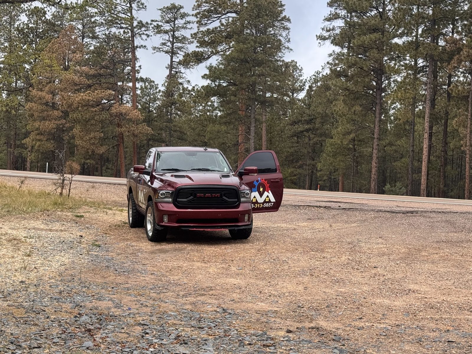 The branded Mendoza A/C Solutions pickup parked among ponderosa pines in northern Arizona with the driver's door open.